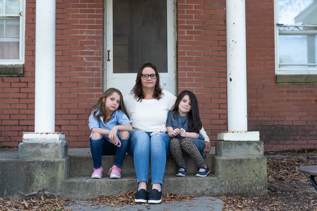 Margaret Szabo, 42, sits with her two daughters on the porch of their home in Richmond, Virginia, on Nov. 6. The Richmond Redevelopment and Housing Authority, which owns Szabo’s home, filed an eviction case against her for unpaid rent last fall. She said an aid organization paid the back rent, but she’s behind again in 2020. (Nick McMillan/Howard Center)